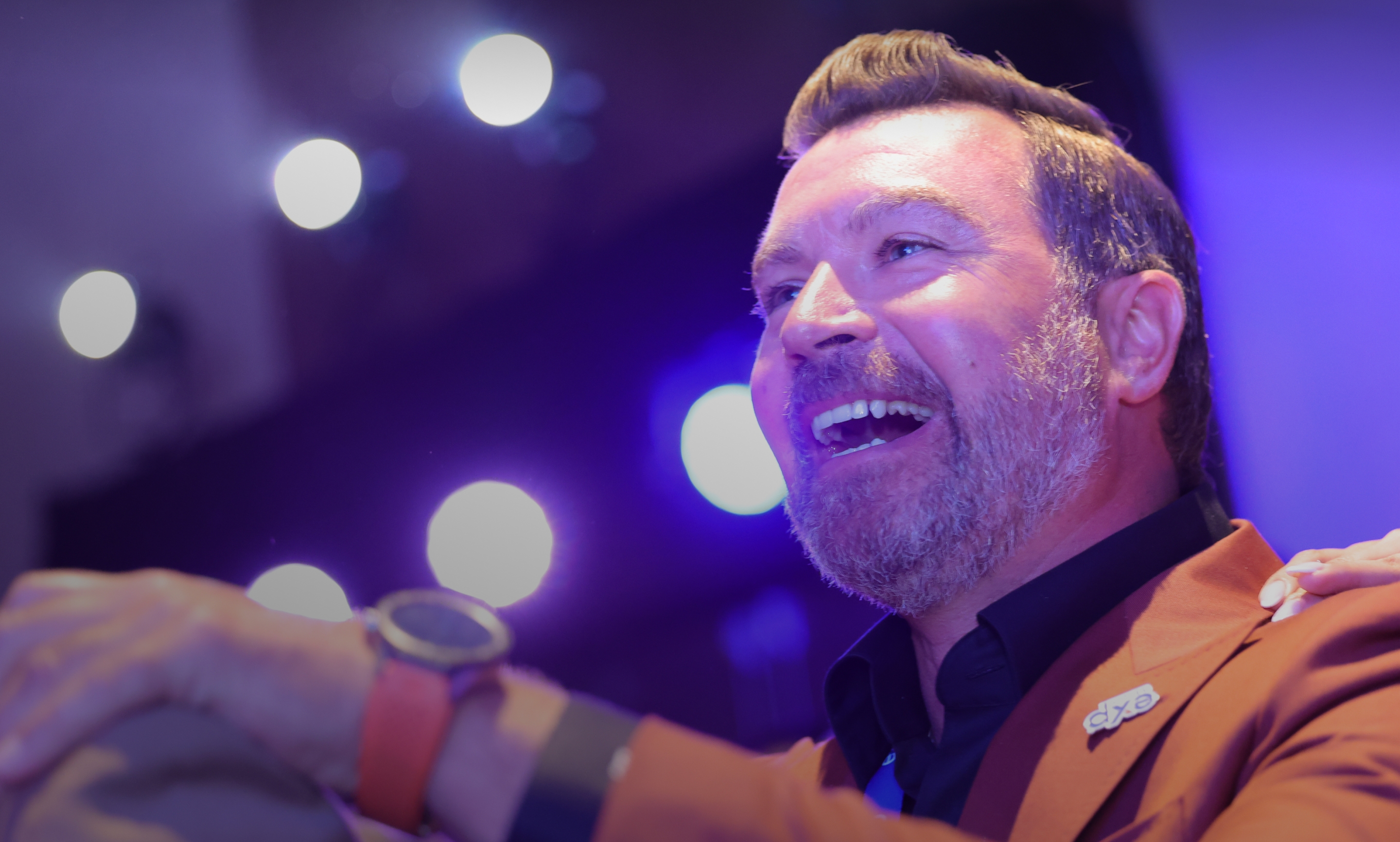 Man in a suit smiling and enjoying an event under bright stage lights.